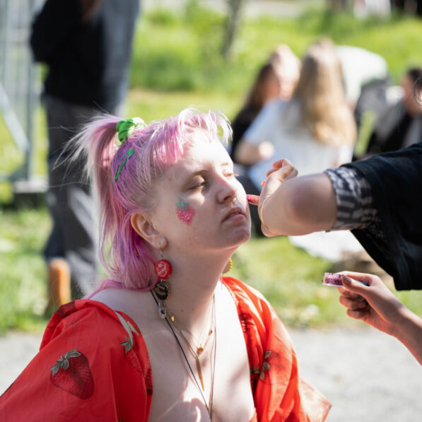 En ung kvinde med lyserødt hår før påført glittermakeup af en anden kvinde.
