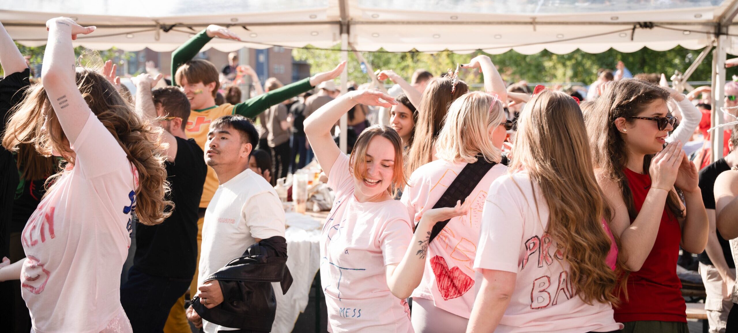 En flok studerende danser samlet i et festivaltelt. Solen skinner og alle er iført farverrige kostumer.