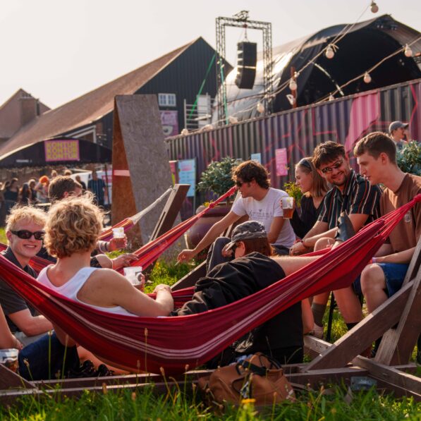 En folk unde mennesker sidder og nyder sommersolen i hængekøjer ved festivalen.