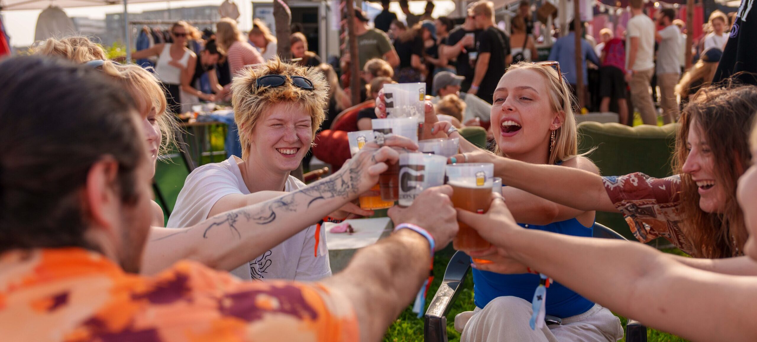 En flok unge mennesker sidder i en cirkel og skåler begejstret med ølglas.