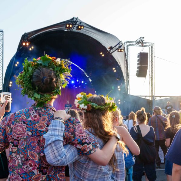 To unge mennesker iført blomsterkranse kigger mod scenen, imens de holder om hinanden.