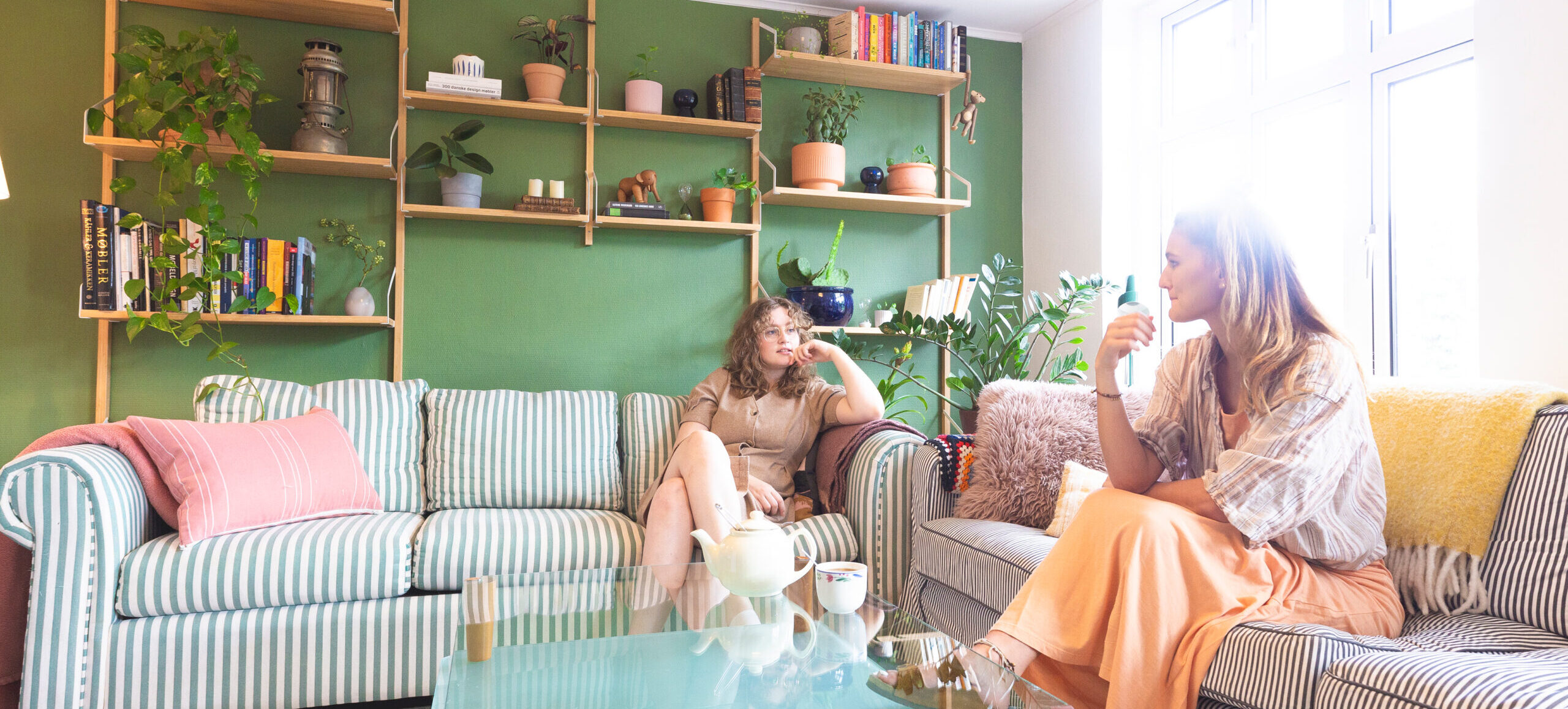 Natascha og Helena sidder i hver sin sofa i deres farverige lejlighed.