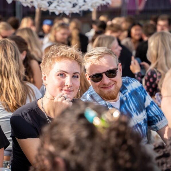 En mand og kvinder sidder ved et bord omgivet af andre mennesker. De smiler begge mod kameraet.