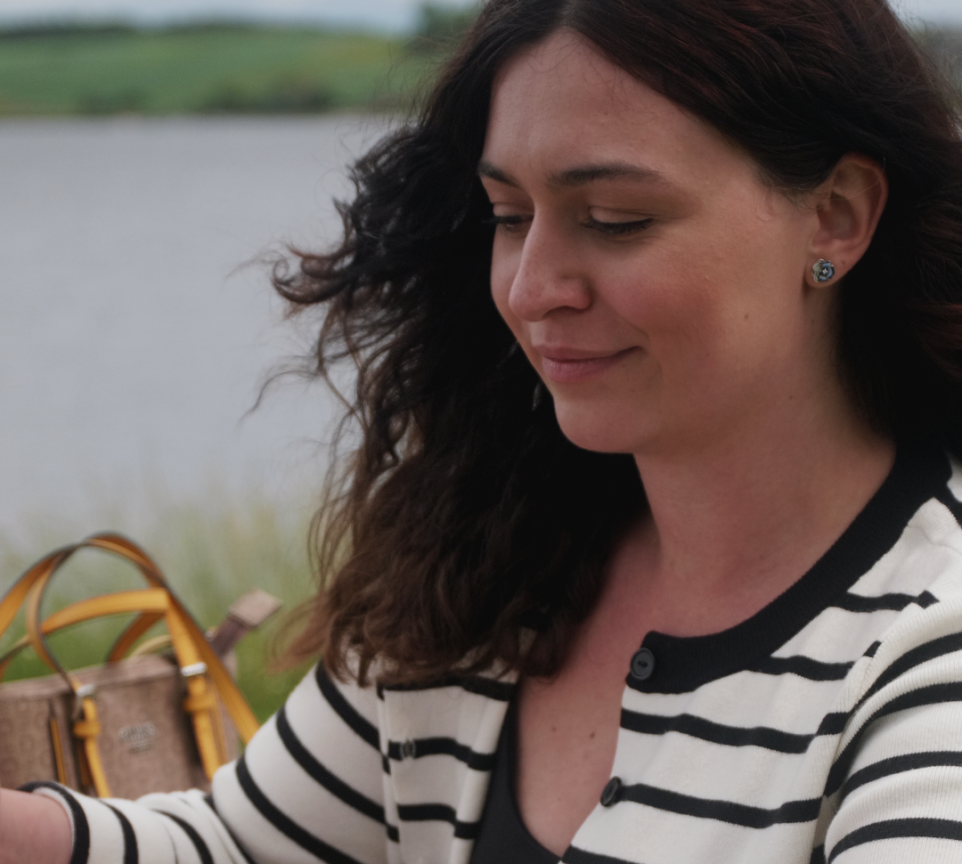 Dragana sidder udenfor med solskin, vind i håret og hav i baggrunden.