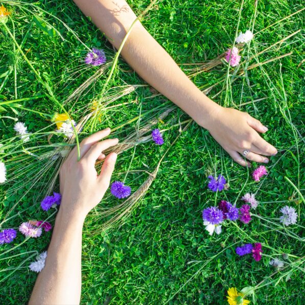 Hænder på græs med blomster strøet omkring