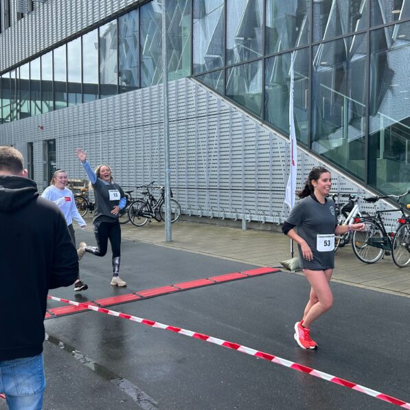 3 unge kvinder smiler og vinker, imens de løber over målstregen.