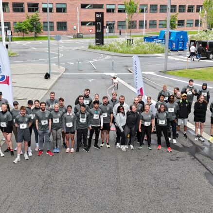 En flok studerende iført grå "Campus Kolding Løb" T-shirts står samlet foran målstregen og kigger mod kameraet.