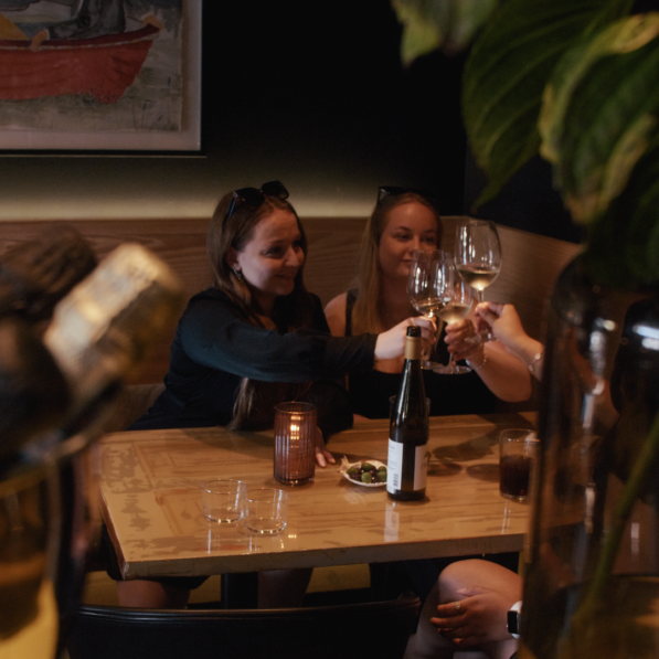 Mette sidder på en mørkbelyst bar og skåler vinglas med to veninder.