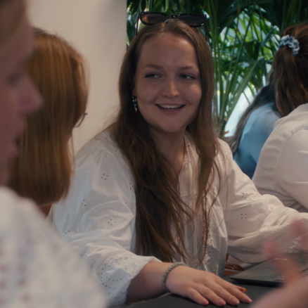 Mette sidder omgivet af andre unge mennesker. Hun snakker smilende med kvinden til sin højre.