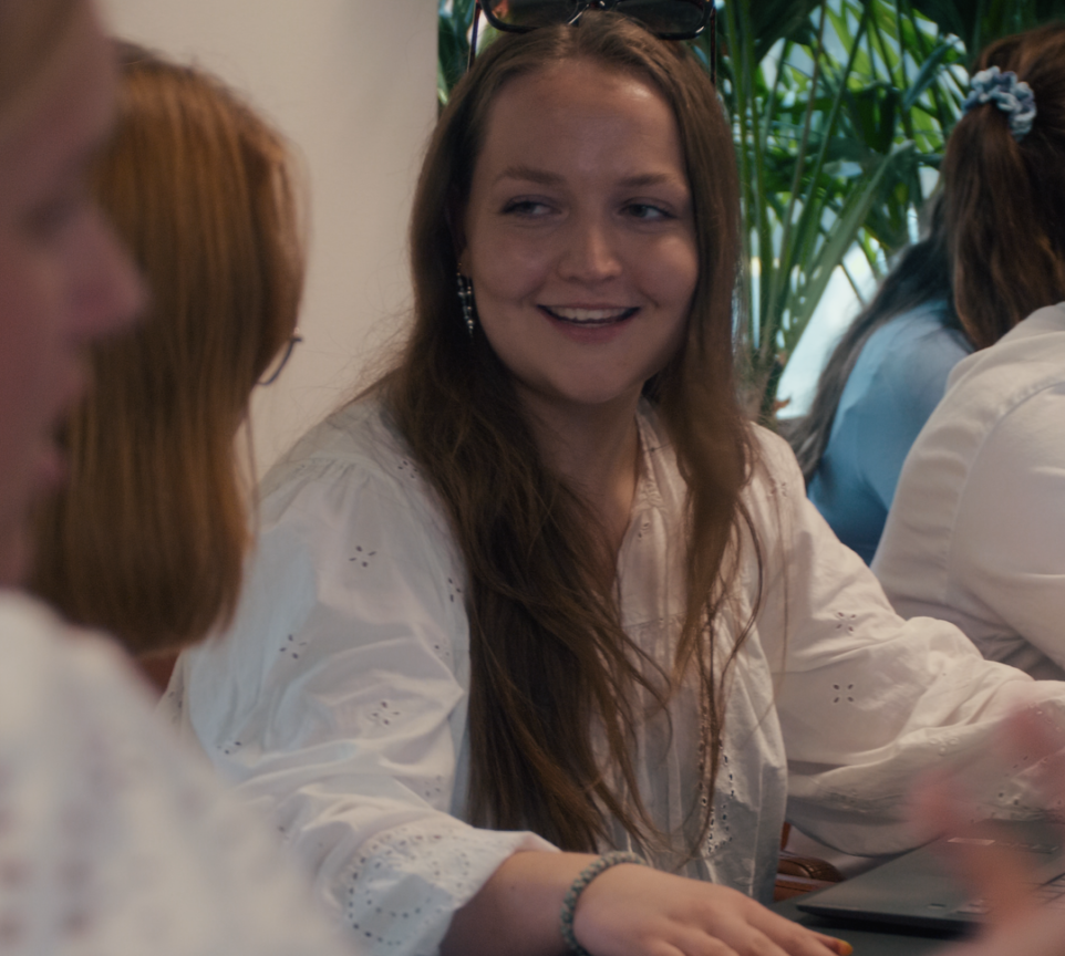 Mette sidder omgivet af andre unge mennesker. Hun snakker smilende med kvinden til sin højre.