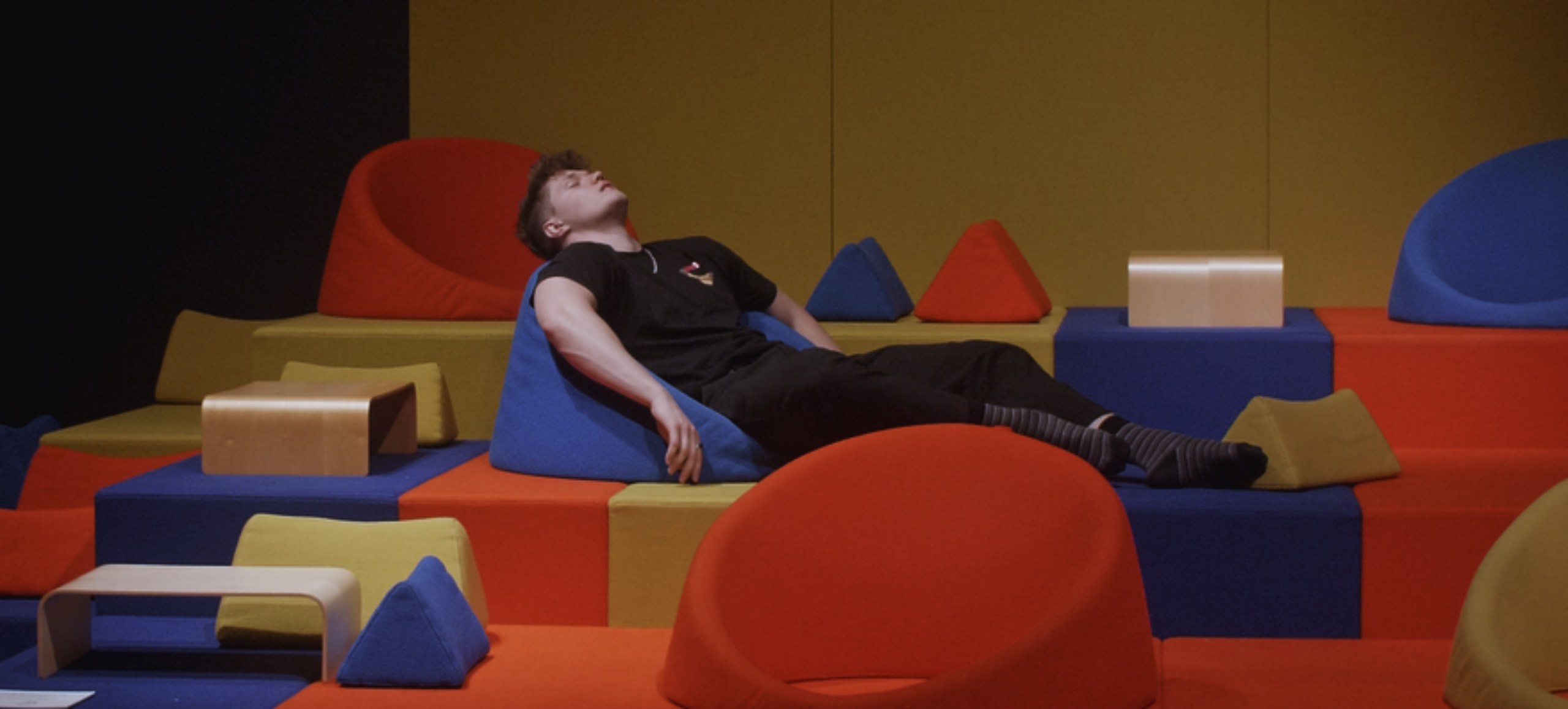 Tobias ligger afslappende i nogle farverige møbler ved kunstmuseum Trapholt.