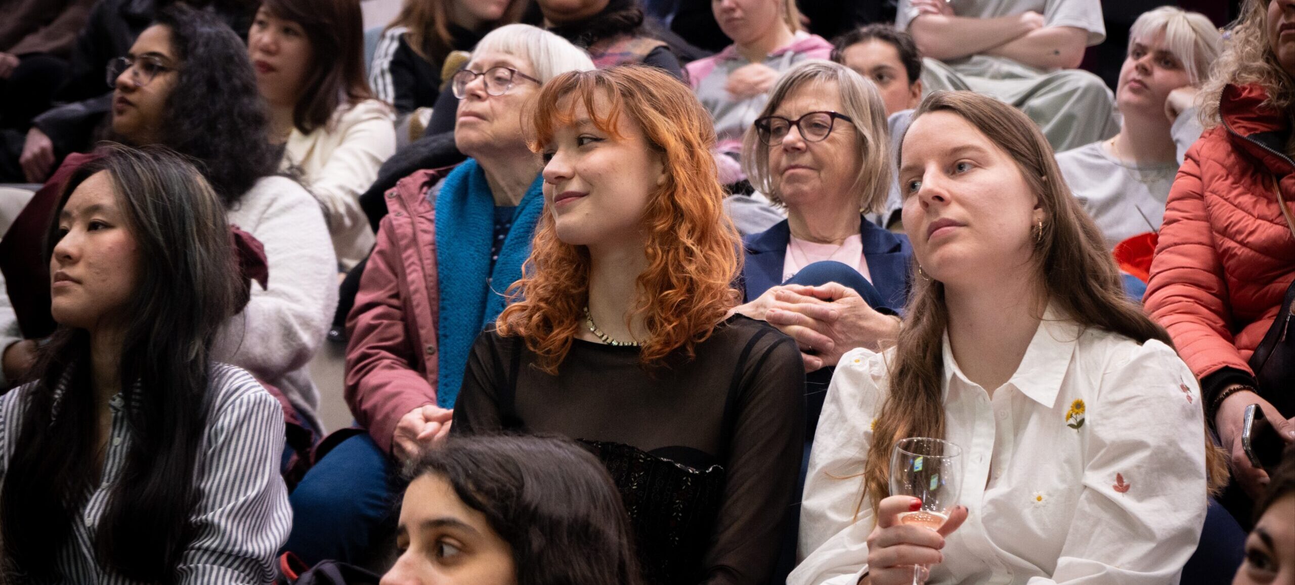 Publikummet til Women's Week arrangementet er en blanding af unge og ældre kvinder, som alle sidder og lytter til Sofie Riise Nors, der er udenfor billedet.