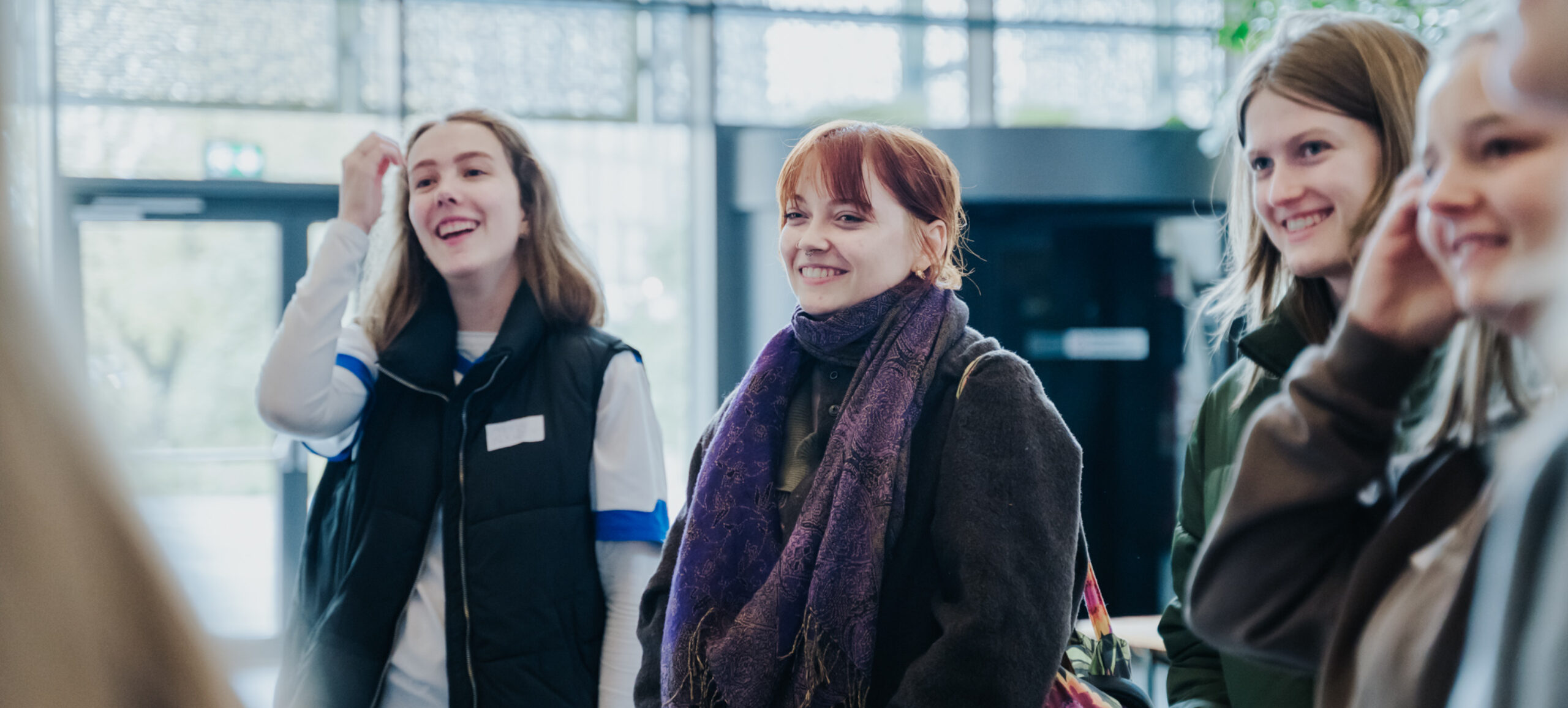 En flok unge, smilende kvinder står samlet i indgangen ved SDU.