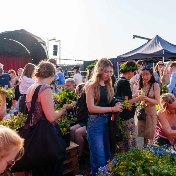En gruppe unge mennesker står på Kontur festivalspladsen og binder blomsterkranse smukke røde og orange blomster.